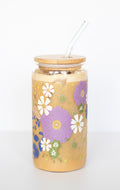Can glass with a purple anemone and white daisy floral design against a white background. 