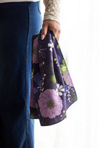 Person holding a floral-patterned navy waffle-weave kitchen tea towel against a white background.