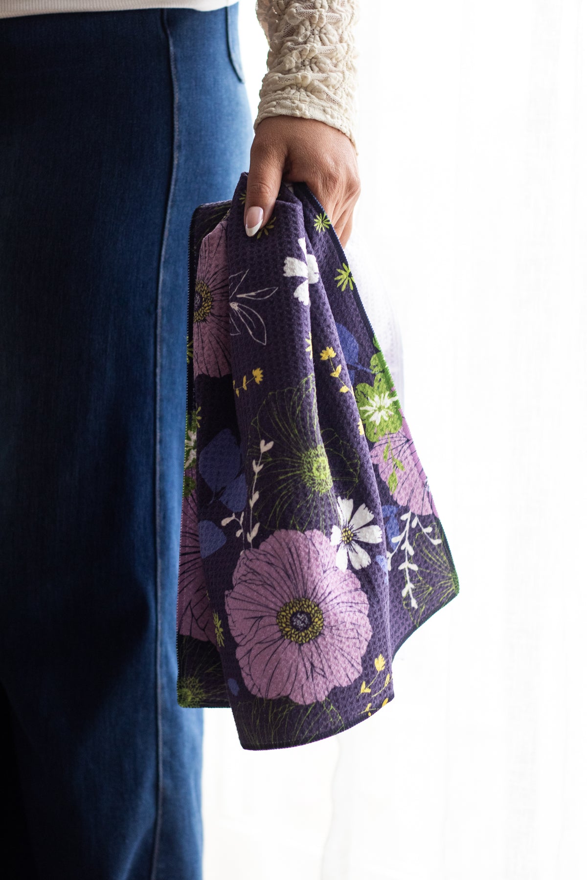 Person holding a floral-patterned navy waffle-weave kitchen tea towel against a white background.