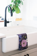 White farmhouse kitchen sink with a black faucet and a floral waffle-weave kitchen tea towel hanging on the side.