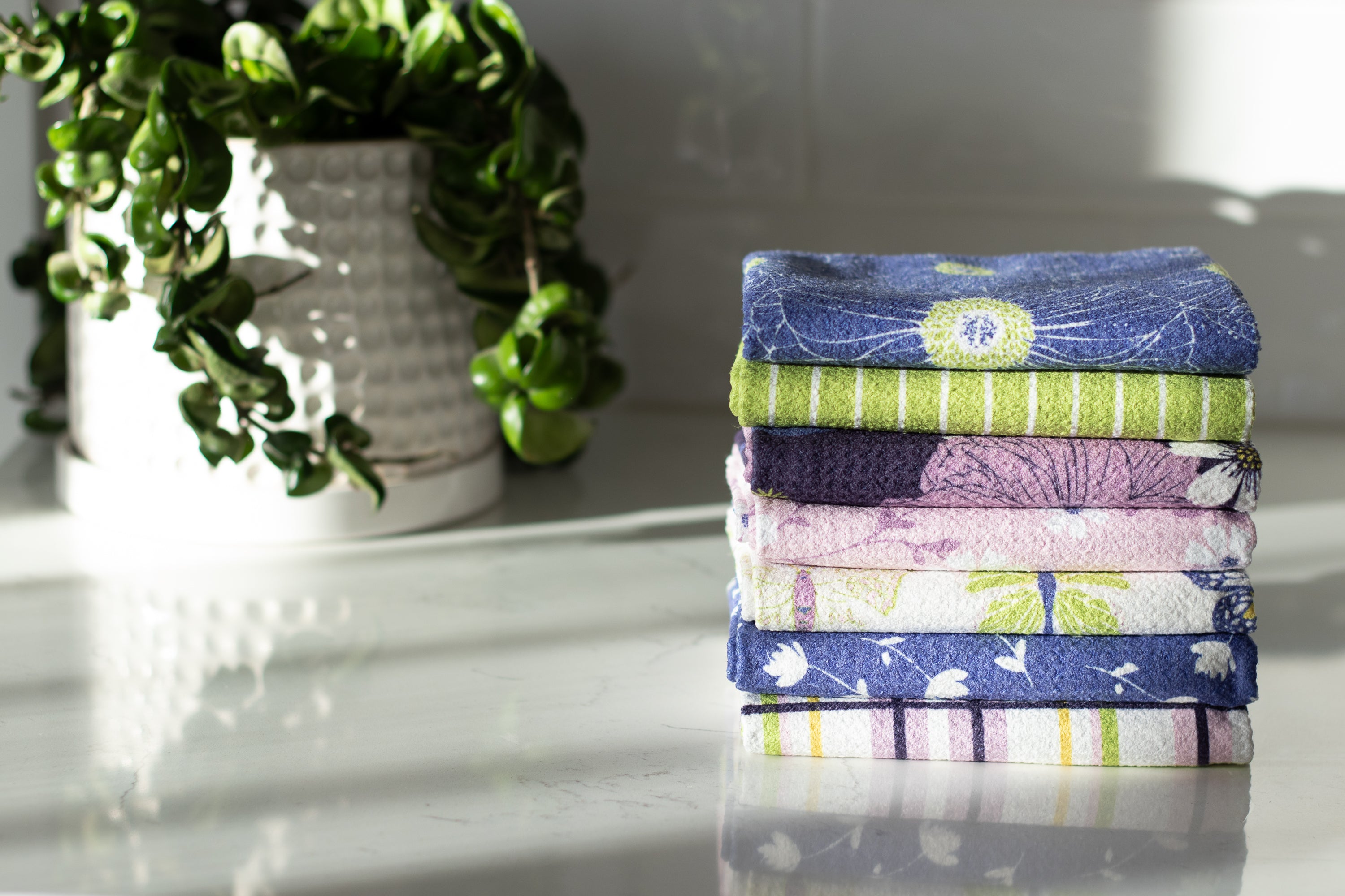 Stack of spring waffle-weave kitchen towels on a white surface with a plant in the background
