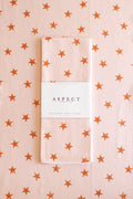 A folded waffle-weave kitchen tea towel with a light pink and brown distressed star pattern, wrapped in a white paper belly band labeled 'ASPECT HOME GOODS', set against a matching patterned background.