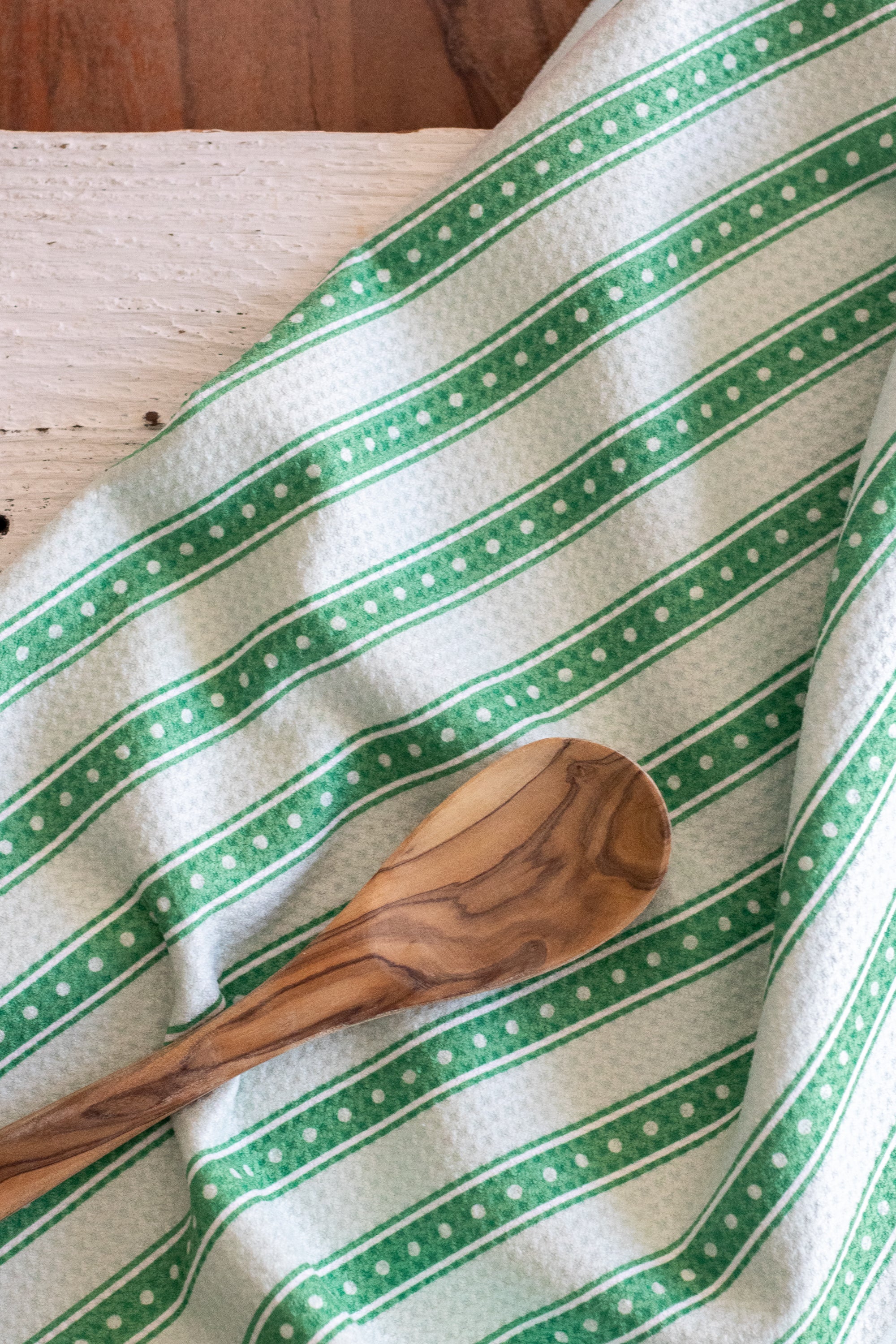 A close-up of a green and white striped kitchen towel with a waffle texture, featuring a wooden spoon resting on it.