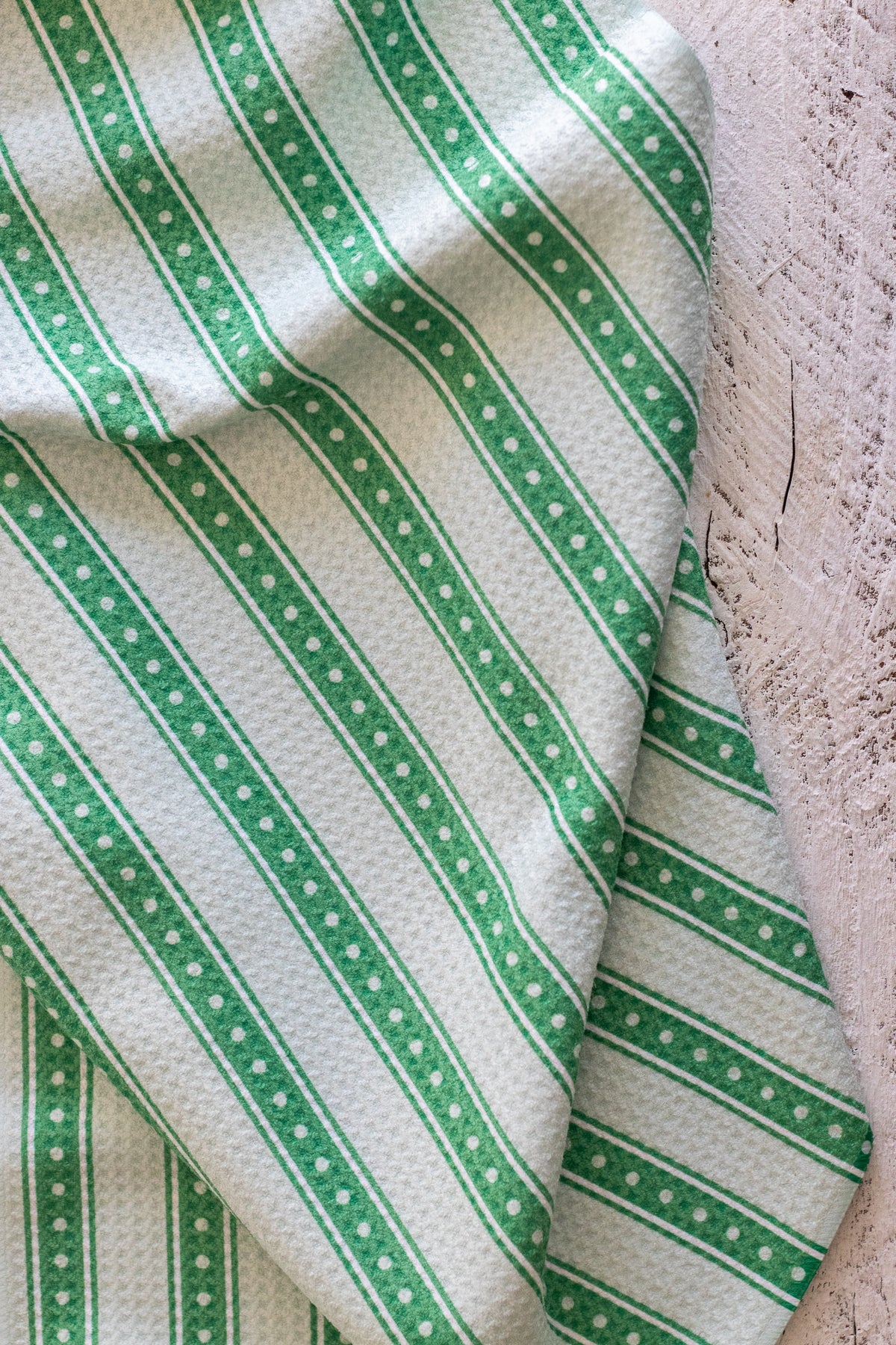 A close-up of a green and white striped fabric with a waffle-weave texture, draped diagonally across a white textured surface.