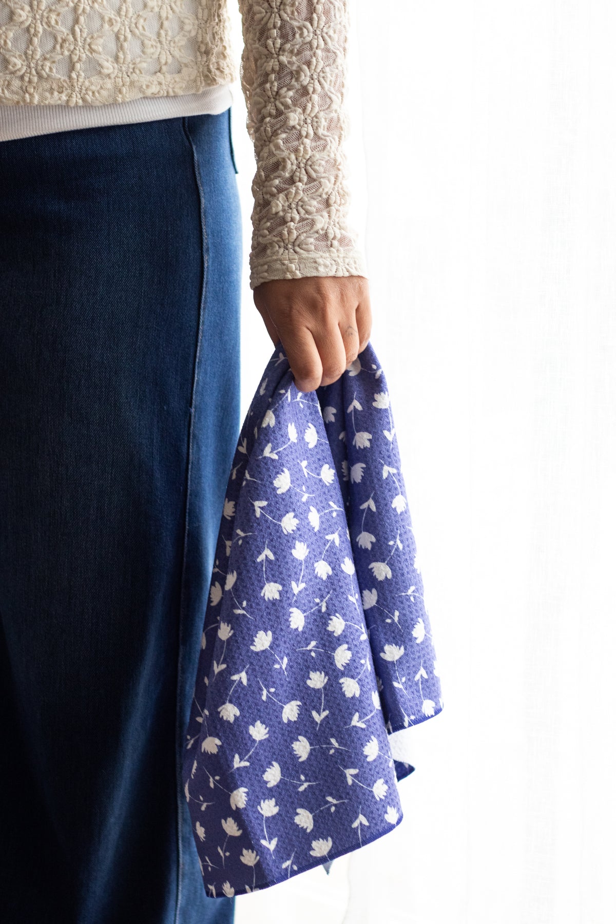 Person holding a waffle-weave kitchen tea towel fabric with a white-and-blue floral pattern against a white background.