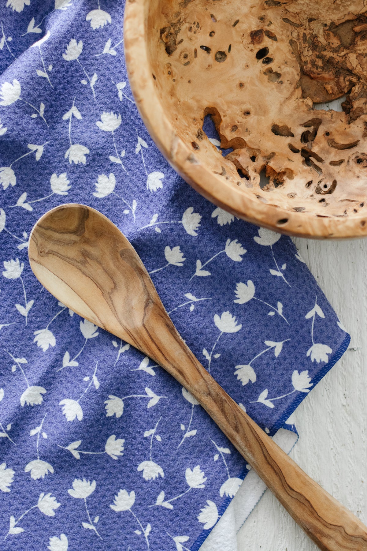 Wooden spoon and bowl on a blue-and-white floral-patterned waffle-weave kitchen tea towel, on a textured white surface.
