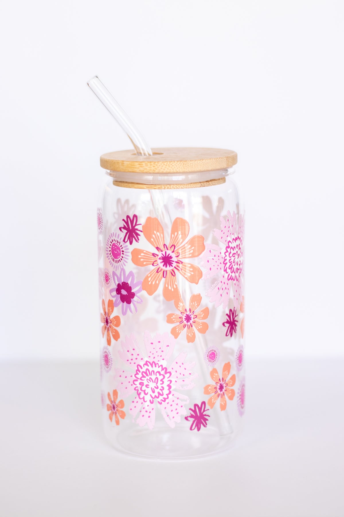 A can glass with a colorful floral design in pink, orange, and purple with a wooden lid and glass straw against a white background.