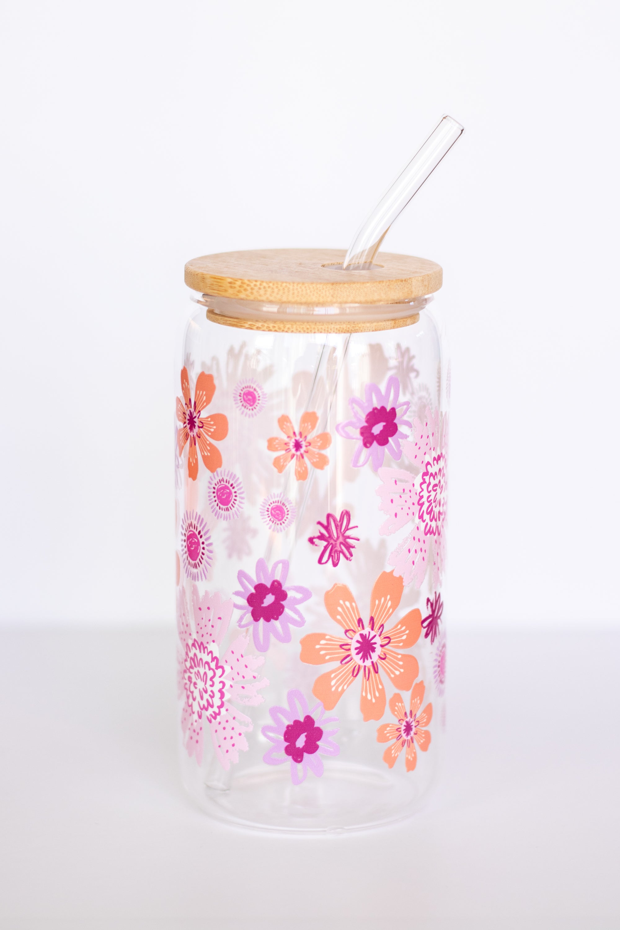 A can glass with a colorful floral design in pink, orange, and purple with a wooden lid and glass straw against a white background.
