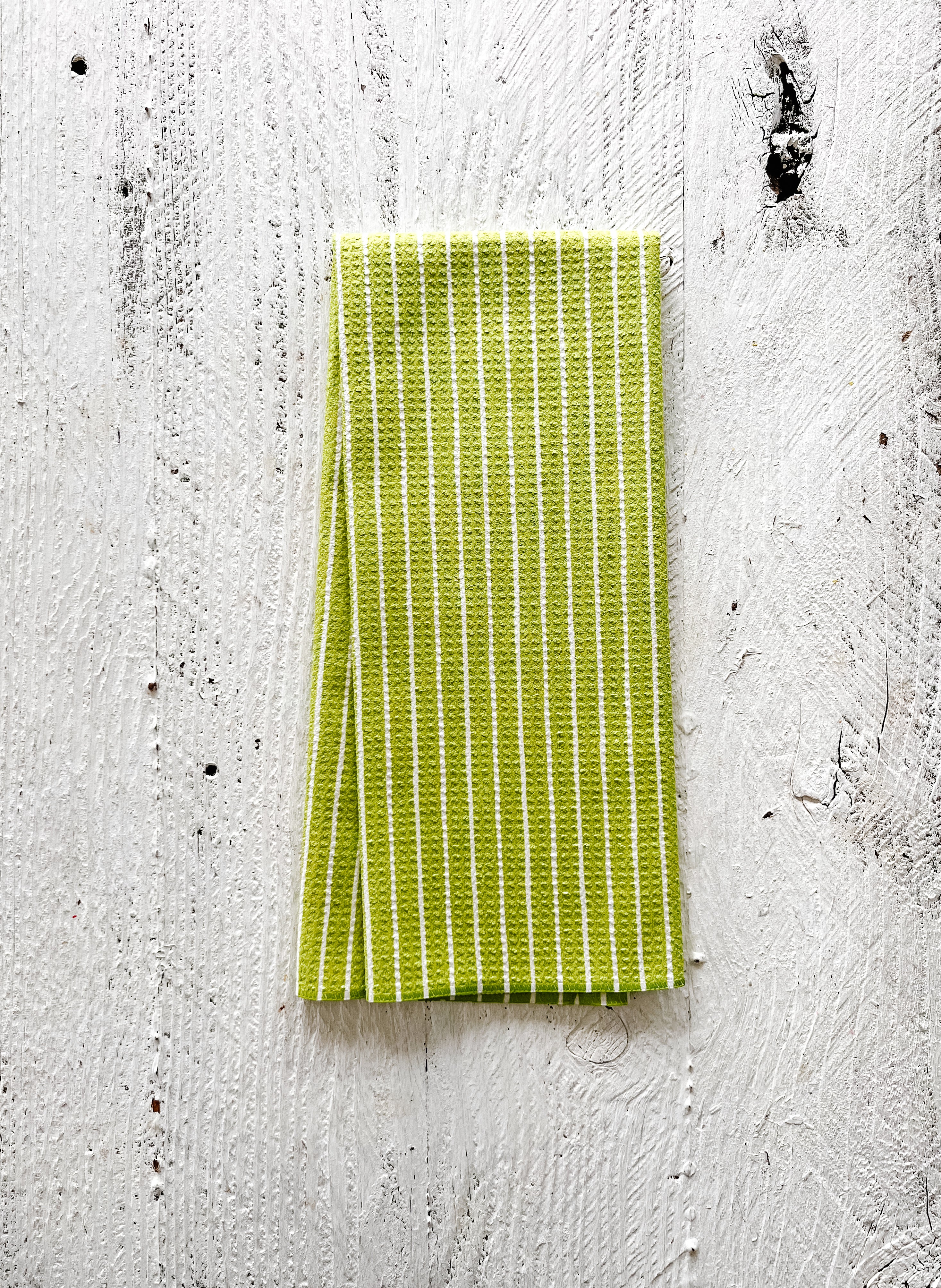 Green striped waffle-weave kitchen towel on a textured white surface