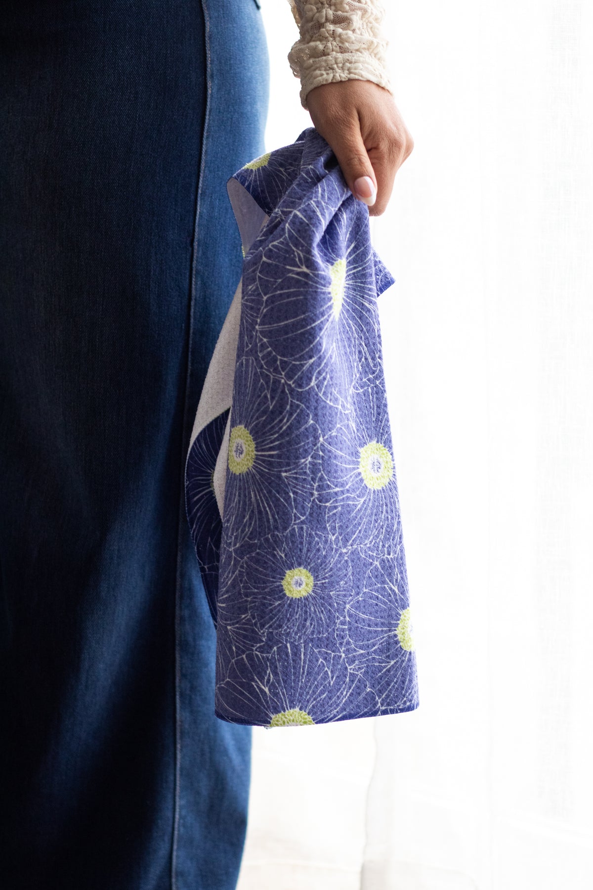 Person holding a waffle-weave kitchen tea towel with a hand-drawn anemone floral pattern in lime green and blue against a white background.
