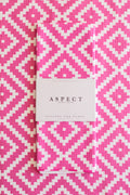 A folded kitchen tea towel with a pink and white geometric diamond pattern, featuring a white paper belly band that reads 'ASPECT HOME GOODS' and 'Kitchen Tea Towel'. The background is a matching flat-lay of the same tea towel pattern.