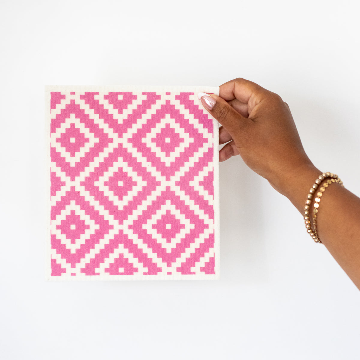 A hand holding a Swedish dishcloth with a pink-and-white geometric diamond pattern.