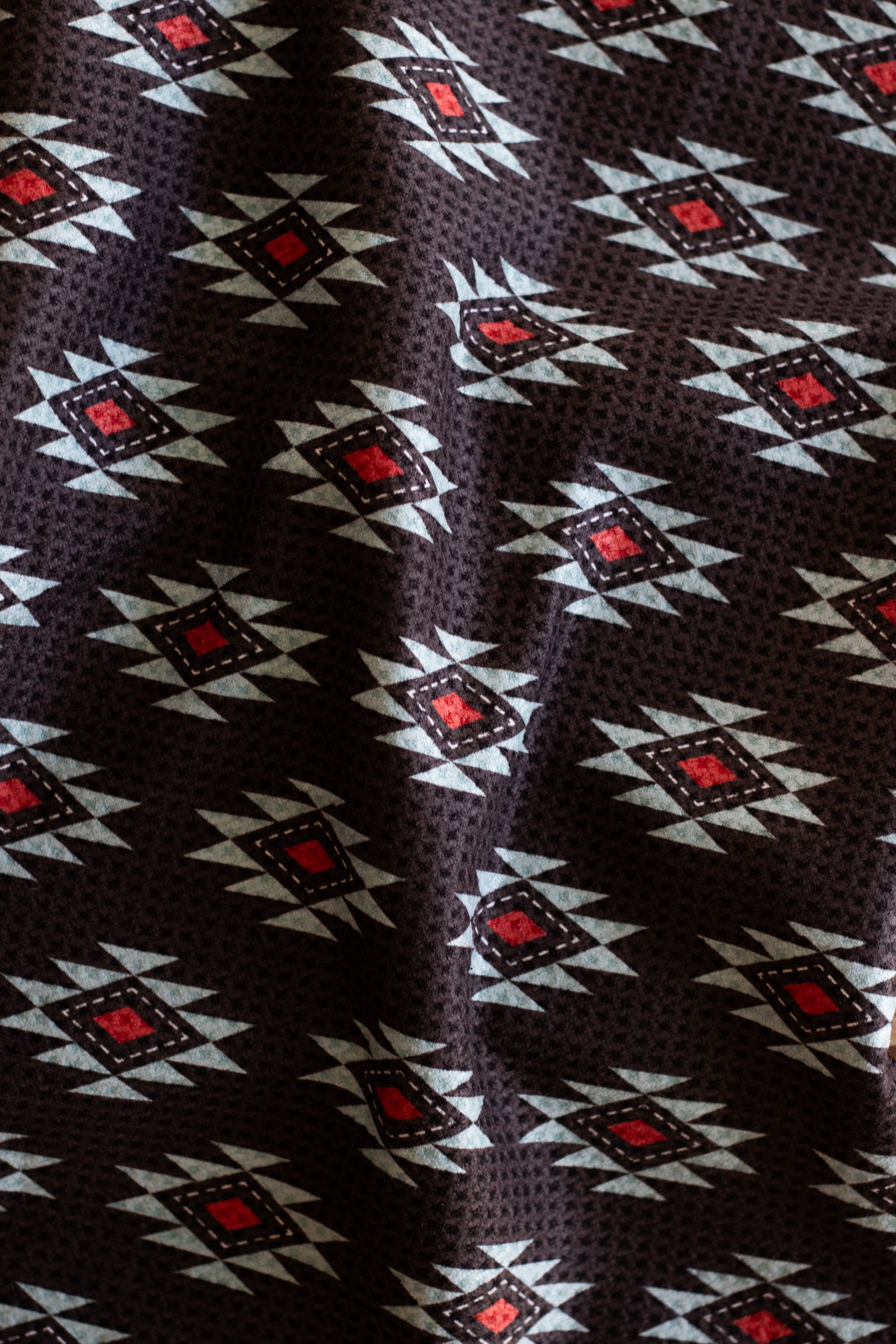 A waffle-weave kitchen tea towel with a Southwestern geometric pattern in turquoise, red, and white, on a black background