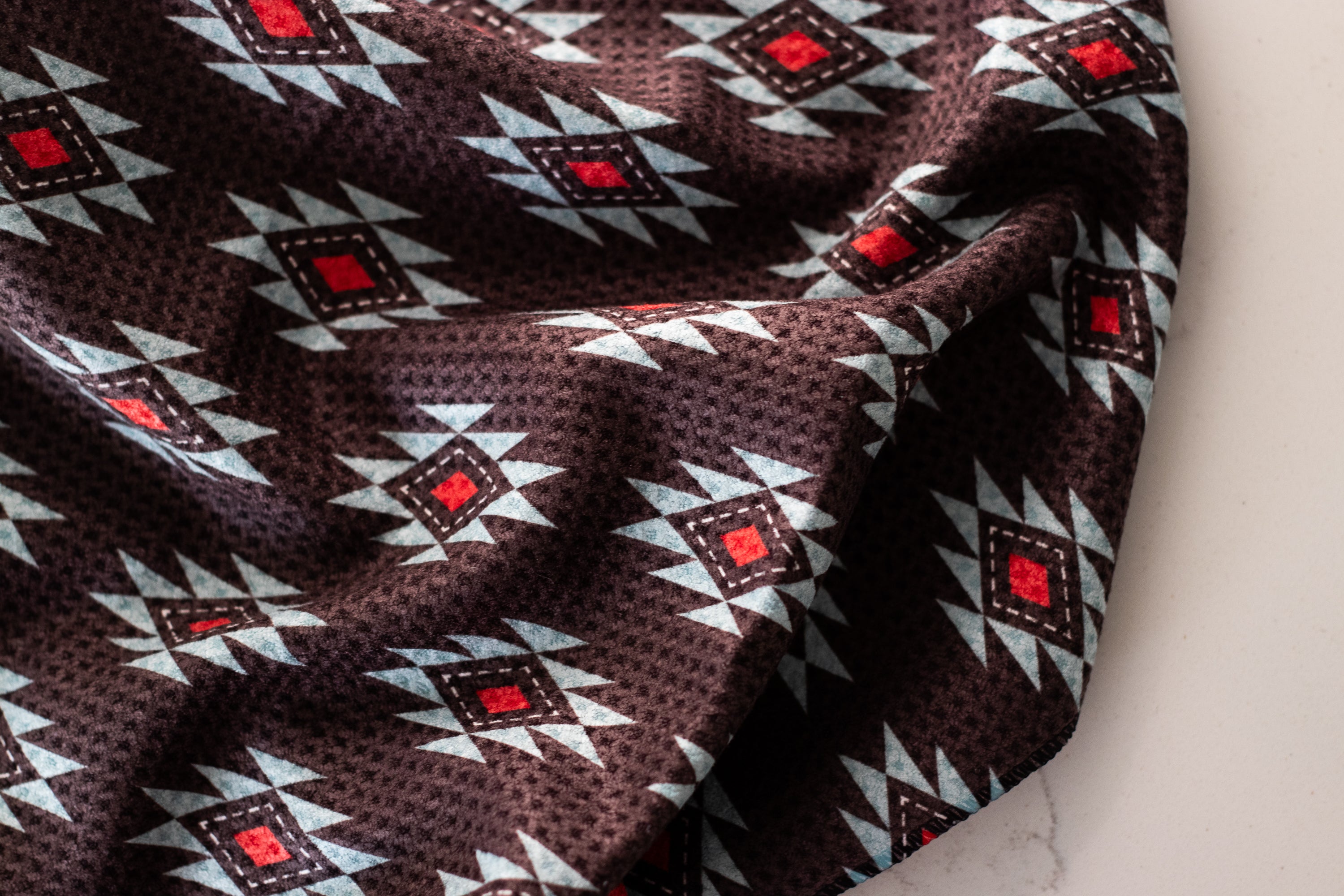 A waffle-weave kitchen tea towel with a Southwestern geometric pattern in turquoise, red, and white, and a black background on a white surface.