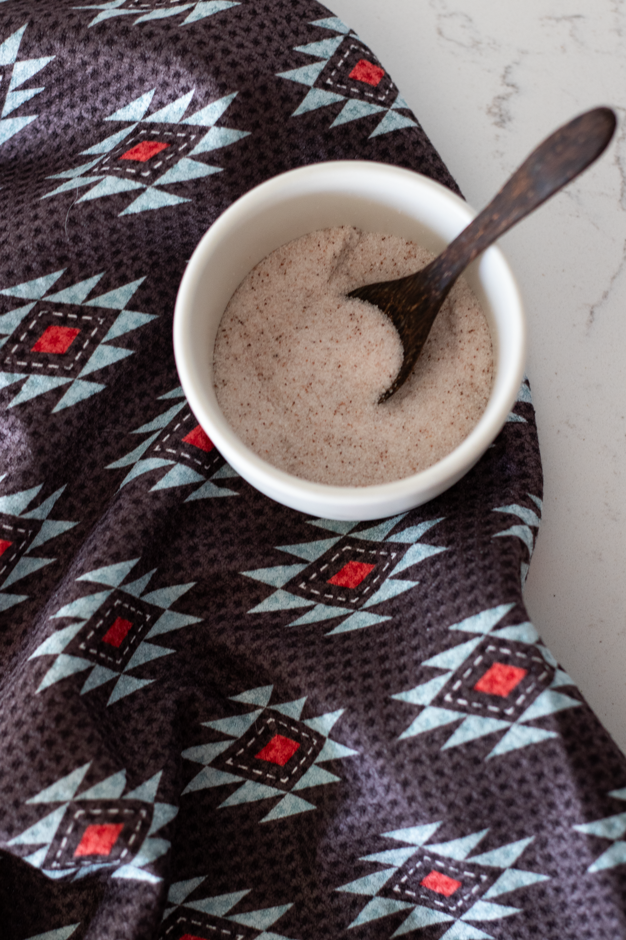 A waffle-weave kitchen tea towel with a Southwestern geometric pattern in turquoise, red, and white, on a black background with a jar of salt, on a white surface