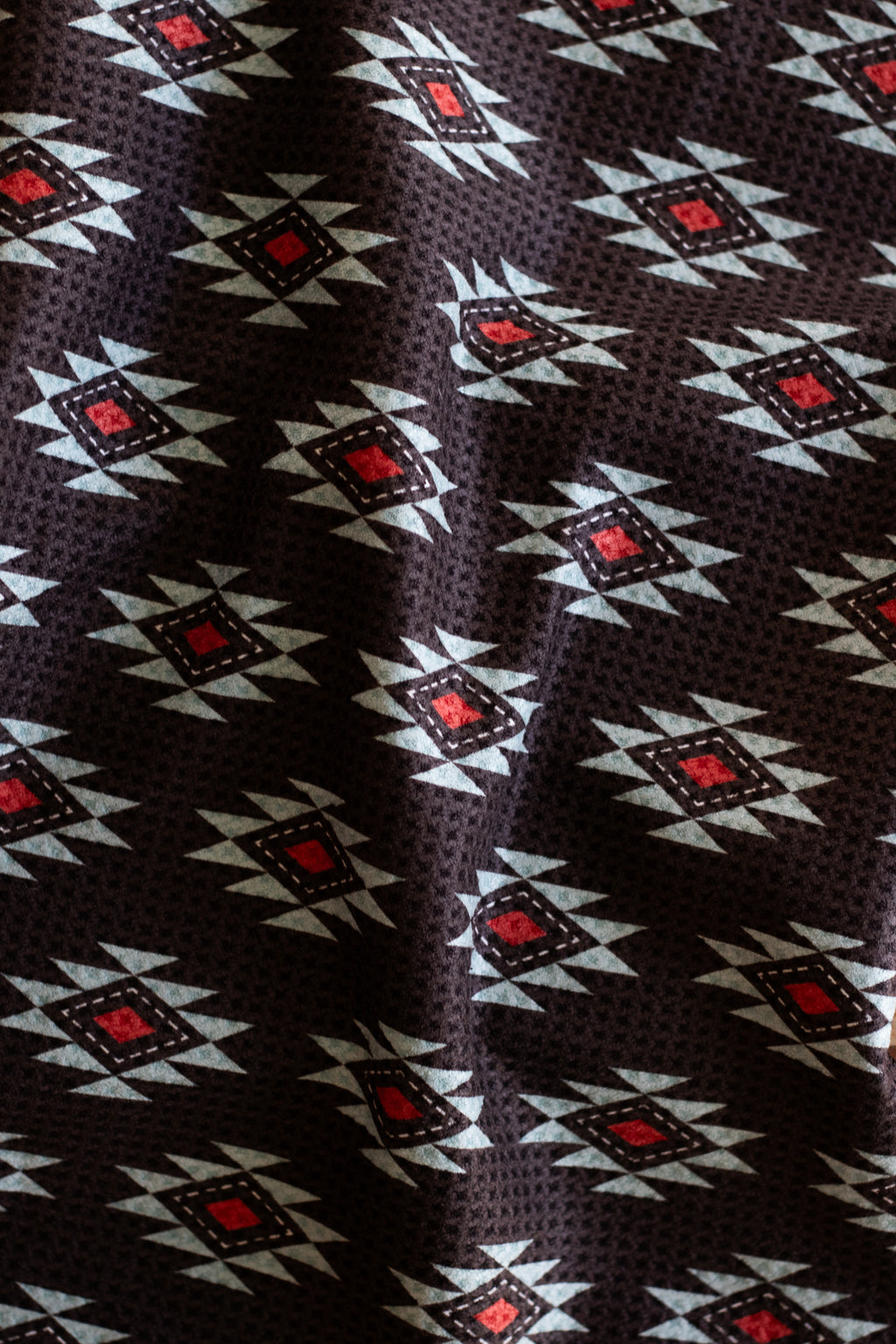 Waffle weave tea towel with a southwestern geometric pattern in turquoise, red, and white, on a black background