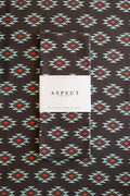 A folded waffle-weave kitchen tea towel with a geometric southwestern-style pattern, featuring a white paper belly band label in the center that reads 'ASPECT HOME GOODS' and 'KITCHEN TEA TOWEL'. The towel has a black background with repeating diamond motifs in turquoise, white, and red.
