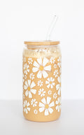 Can glass with white daisy floral pattern, a wooden bamboo lid, and a glass straw, on a white background.