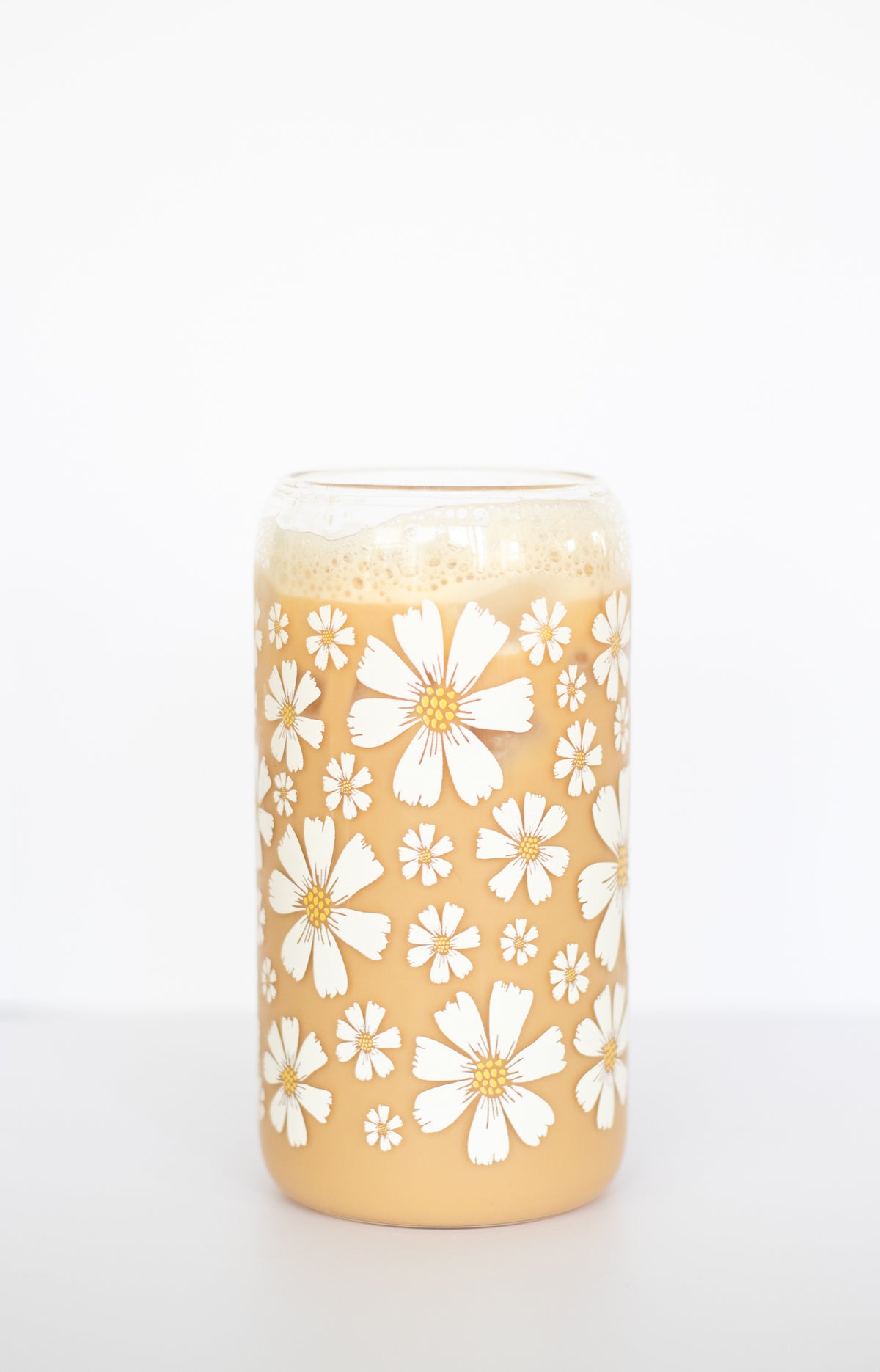 A can glass with a white daisy floral pattern and filled with coffee, on a white background.