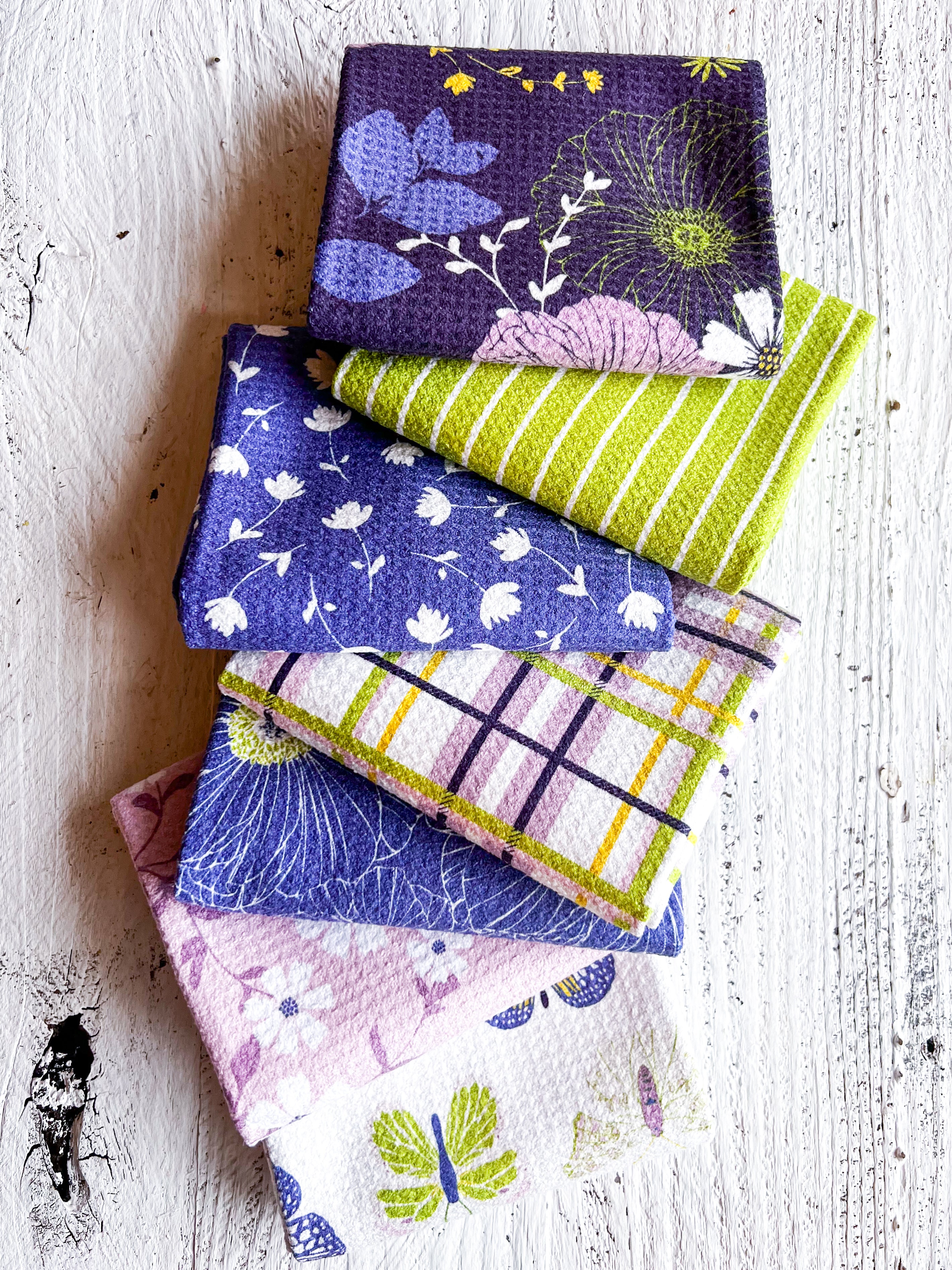 Stack of colorful waffle-weave kitchen tea towels on a white wooden surface.