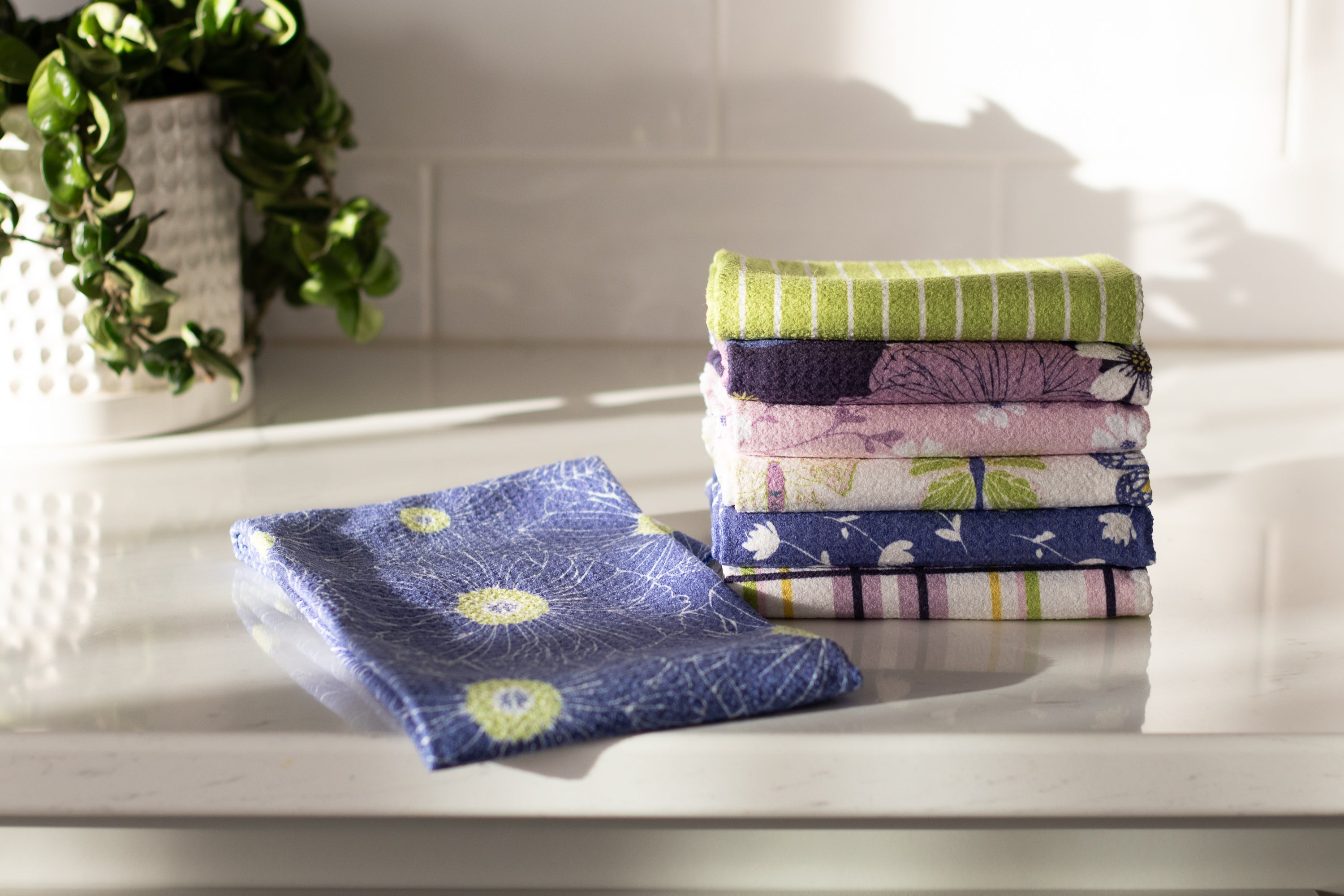 Stack of colorful folded spring towels on a white surface with a plant in the background.