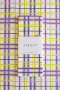 A folded waffle-weave kitchen tea towel with a purple, yellow, lime green, pink and white plaid pattern, wrapped in a white paper belly band labeled 'ASPECT HOME GOODS' and laid flat on a matching plaid background. 