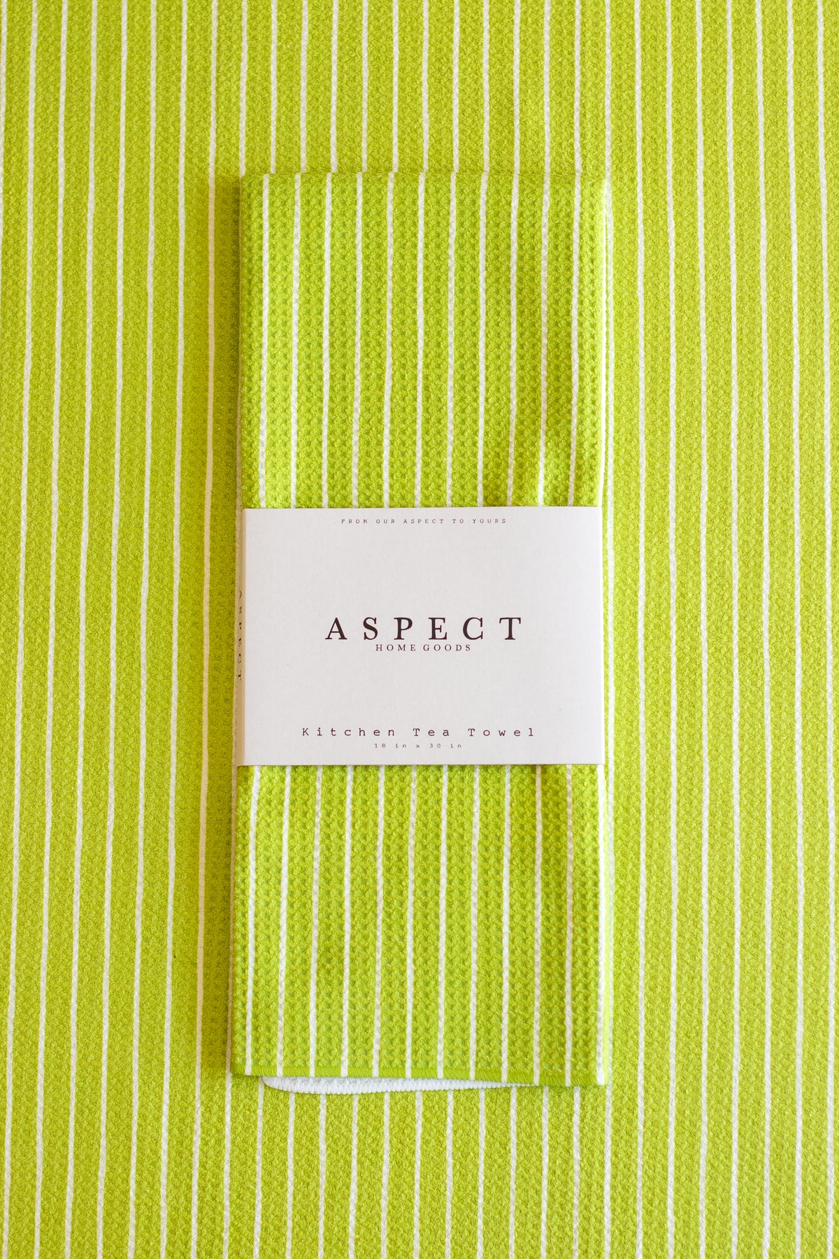A folded kitchen tea towel with a lime green and white vertical stripe pattern, wrapped in a white paper belly band labeled 'ASPECT HOME GOODS' and 'Kitchen Tea Towel'.
