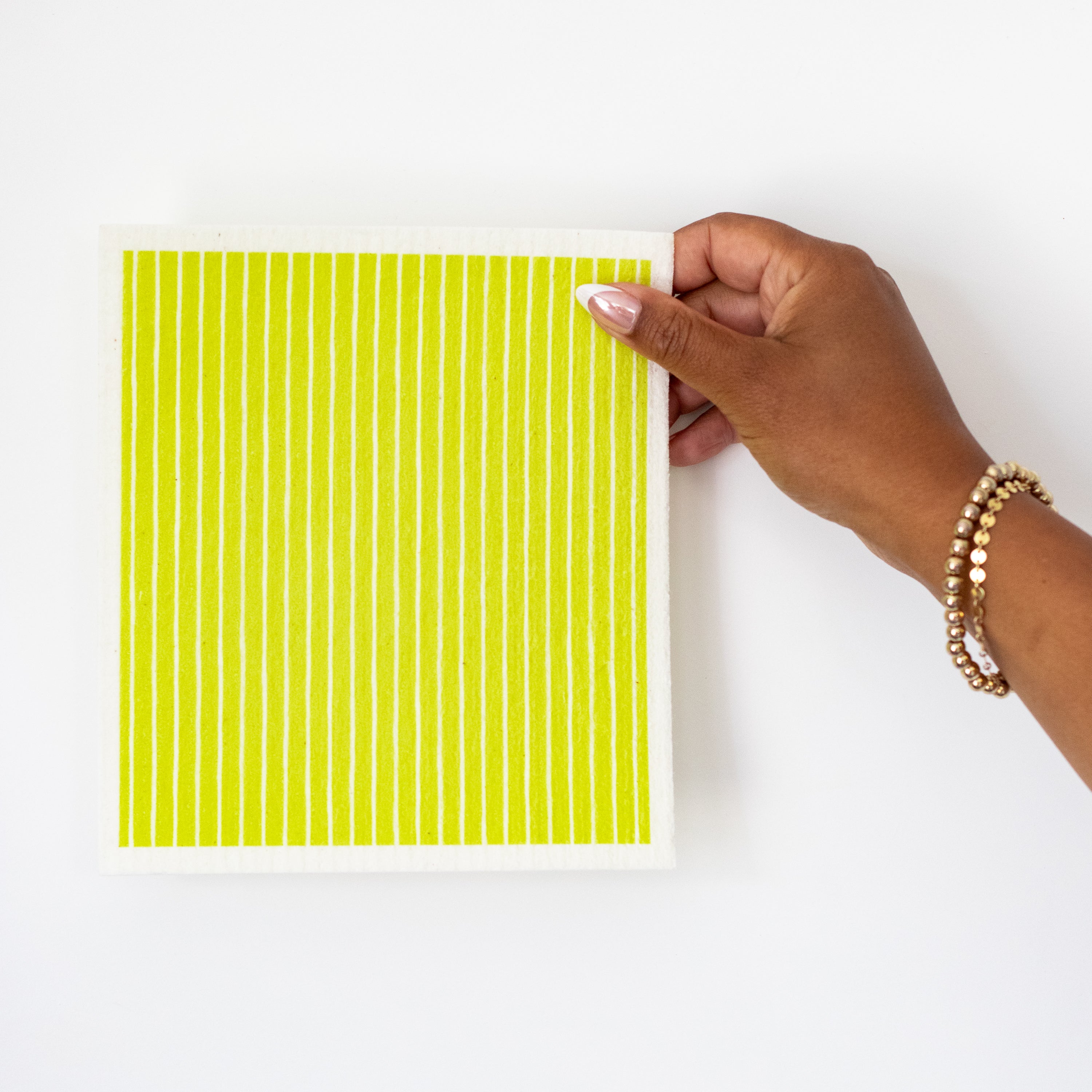 A hand holds a Swedish dishcloth with vertical lime green and white stripes against a plain white background.