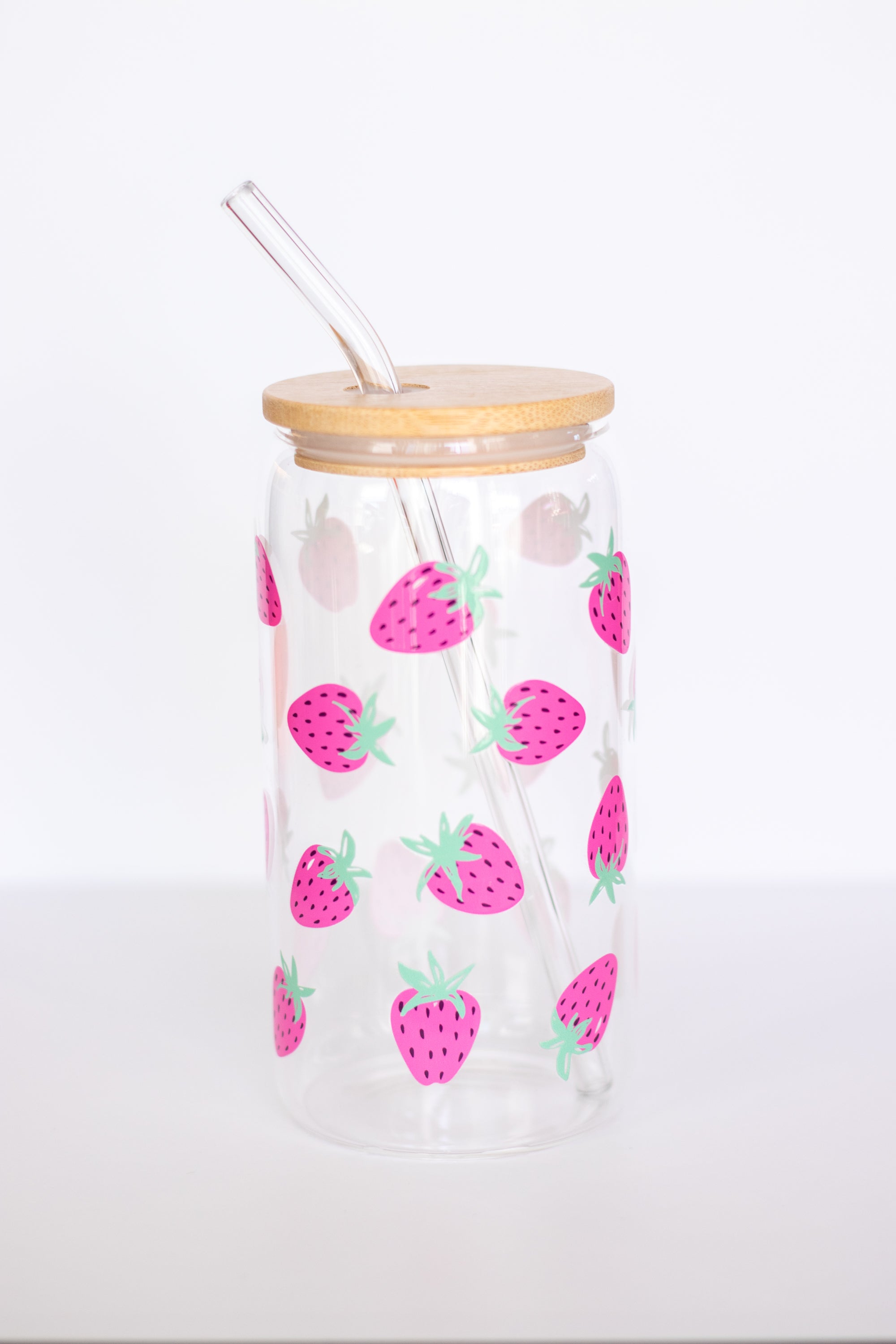Clear can glass tumbler with a hand-painted strawberry pattern, bamboo wooden lid, and a glass straw, against a white background.
