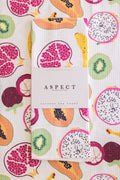 A folded kitchen tea towel with a colorful tropical fruit print is displayed on top of a matching flat tea towel. A white paper belly band around the folded towel reads 'ASPECT HOME GOODS' and 'KITCHEN TEA TOWEL'.