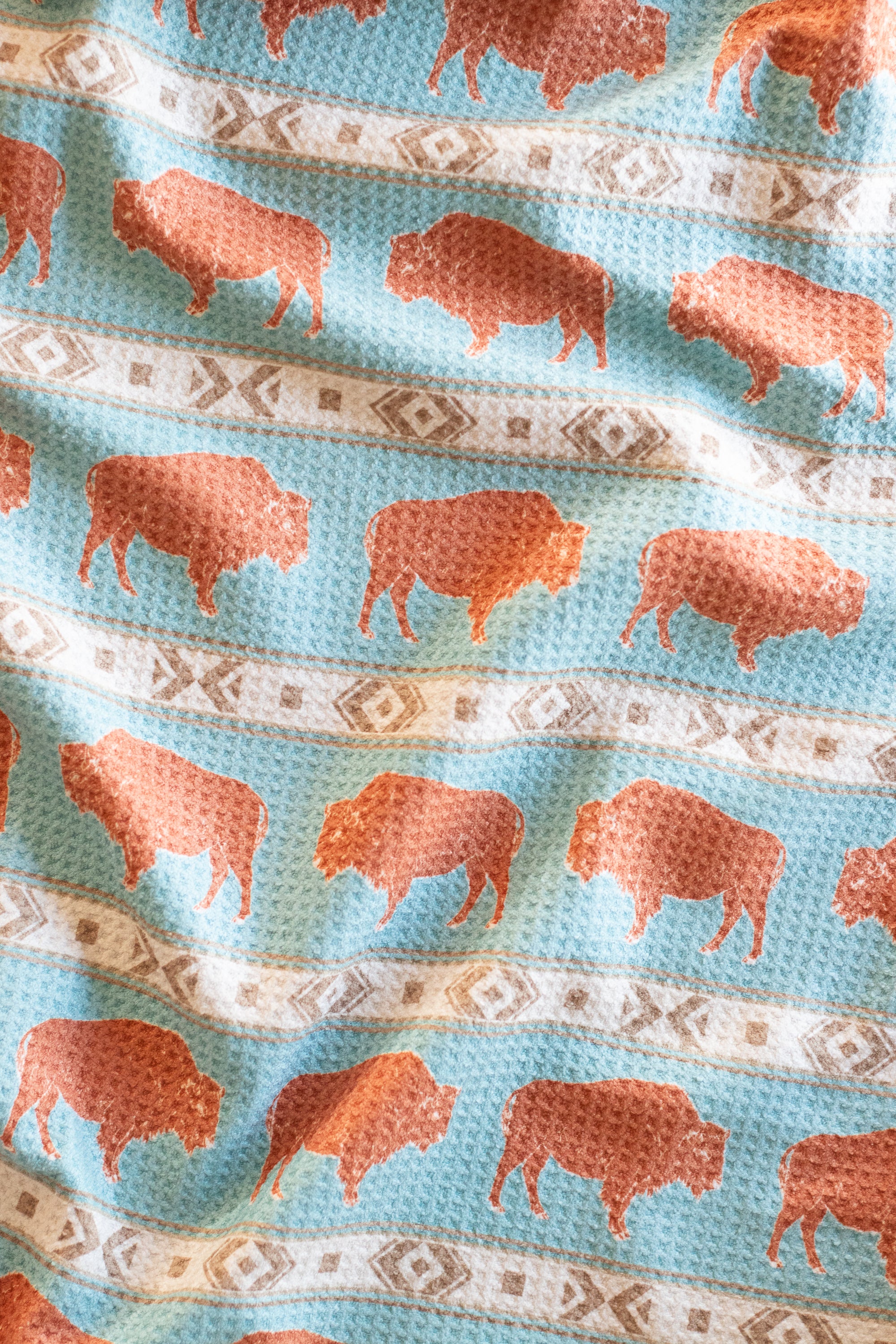 Patterned waffle-weave kitchen tea towel with a terracotta-colored bison and beige southwestern geometric stripe designs on a light blue background