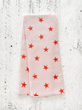 A waffle-weave kitchen tea towel with a pattern of terracotta-colored, distressed stars on a light peachy-pink background, folded lengthwise in half, on a textured white surface.