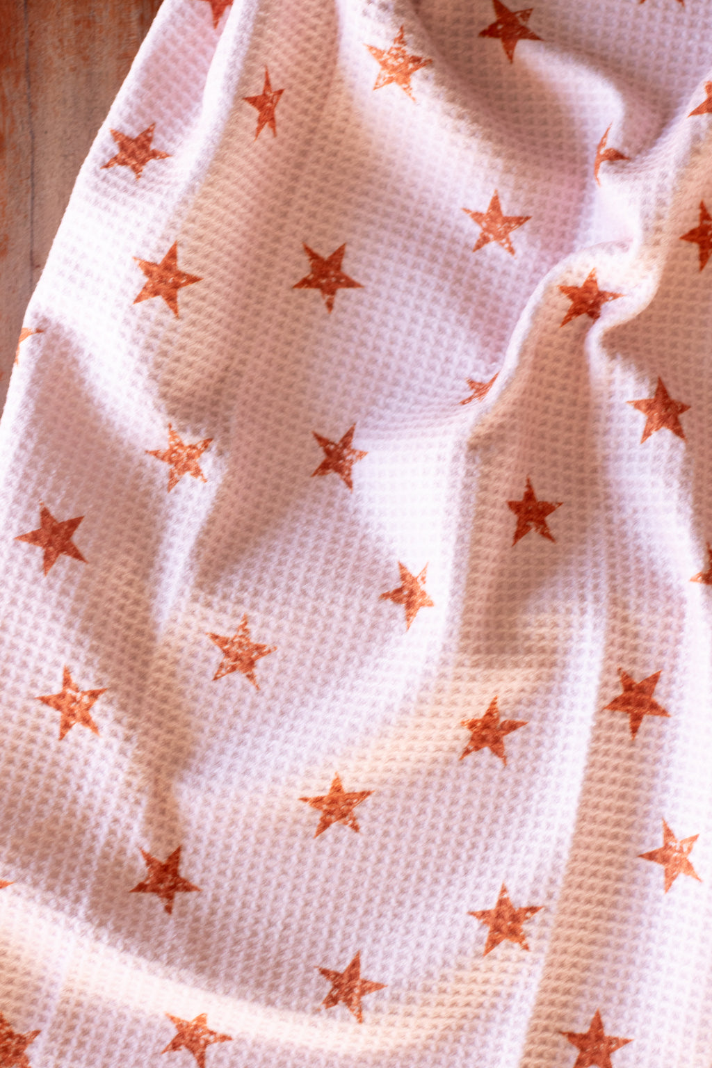 Pink waffle weave tea towel with a distressed brown star pattern on a wooden surface