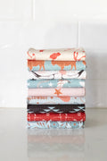 Stack of folded waffle-weave kitchen tea towels with various western patterns and designs on a white surface.