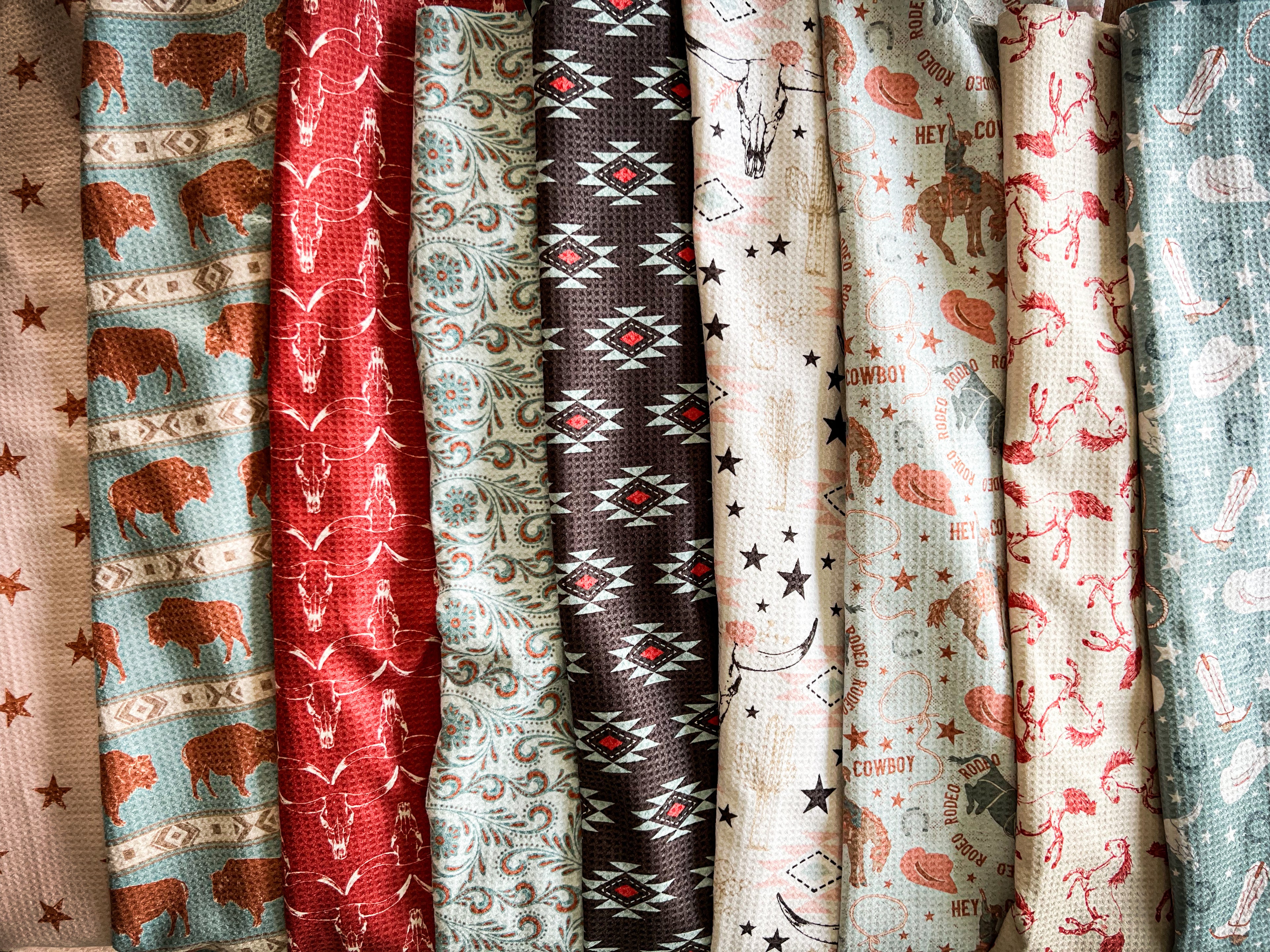 Collection of western-patterned waffle-weave tea towels with various western designs, including animals, geometric shapes, and florals.