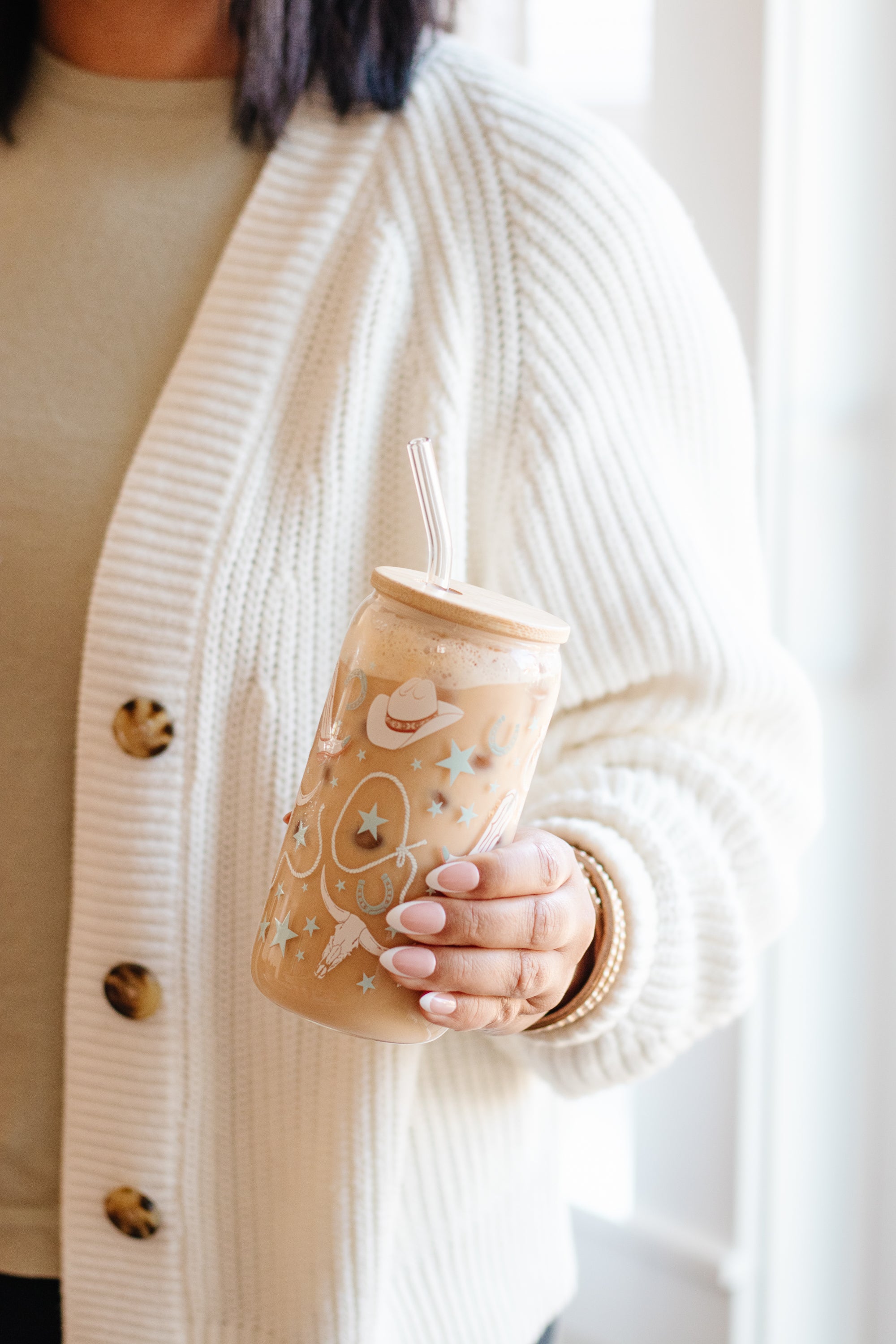 Person holding a can glass with western cowgirl designs against a light background