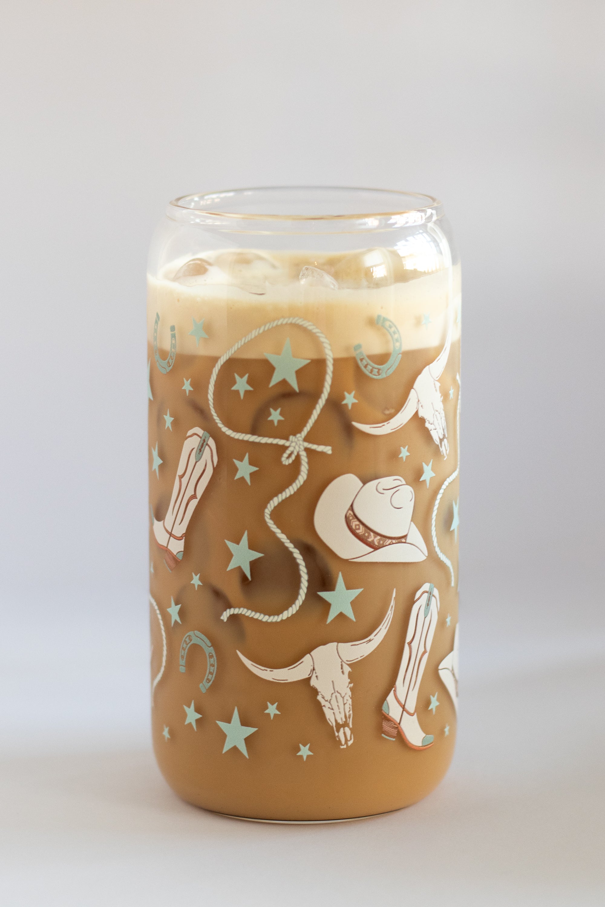 Can glass with a cowgirl-themed design filled with an iced latte on a white background