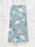 A blue waffle-Weave kitchen tea towel with a cowgirl pattern, including lassos, hats, horseshoes, cow skulls, and stars, on a textured white background.