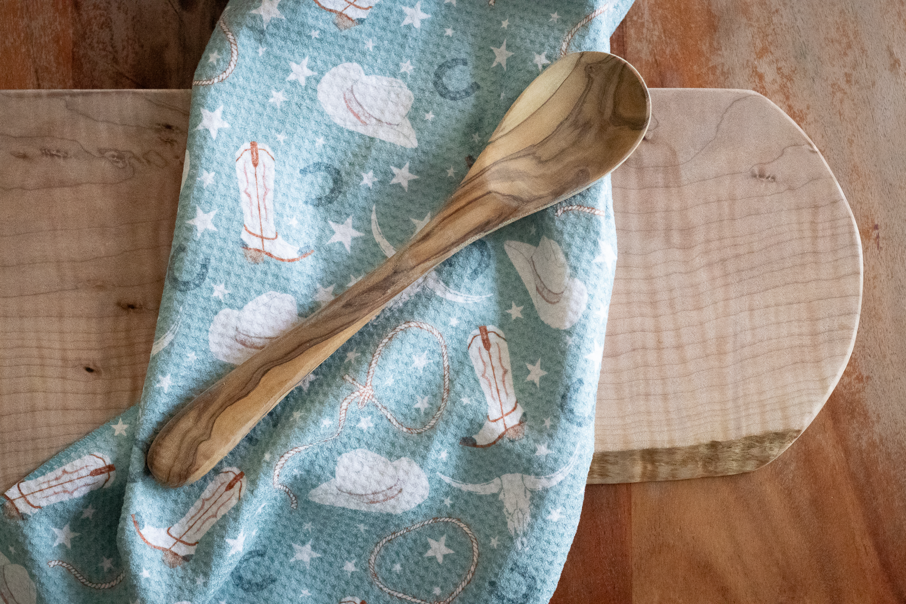 Wooden spoon on a cowgirl-patterned waffle-weave tea towel on a wooden surface.