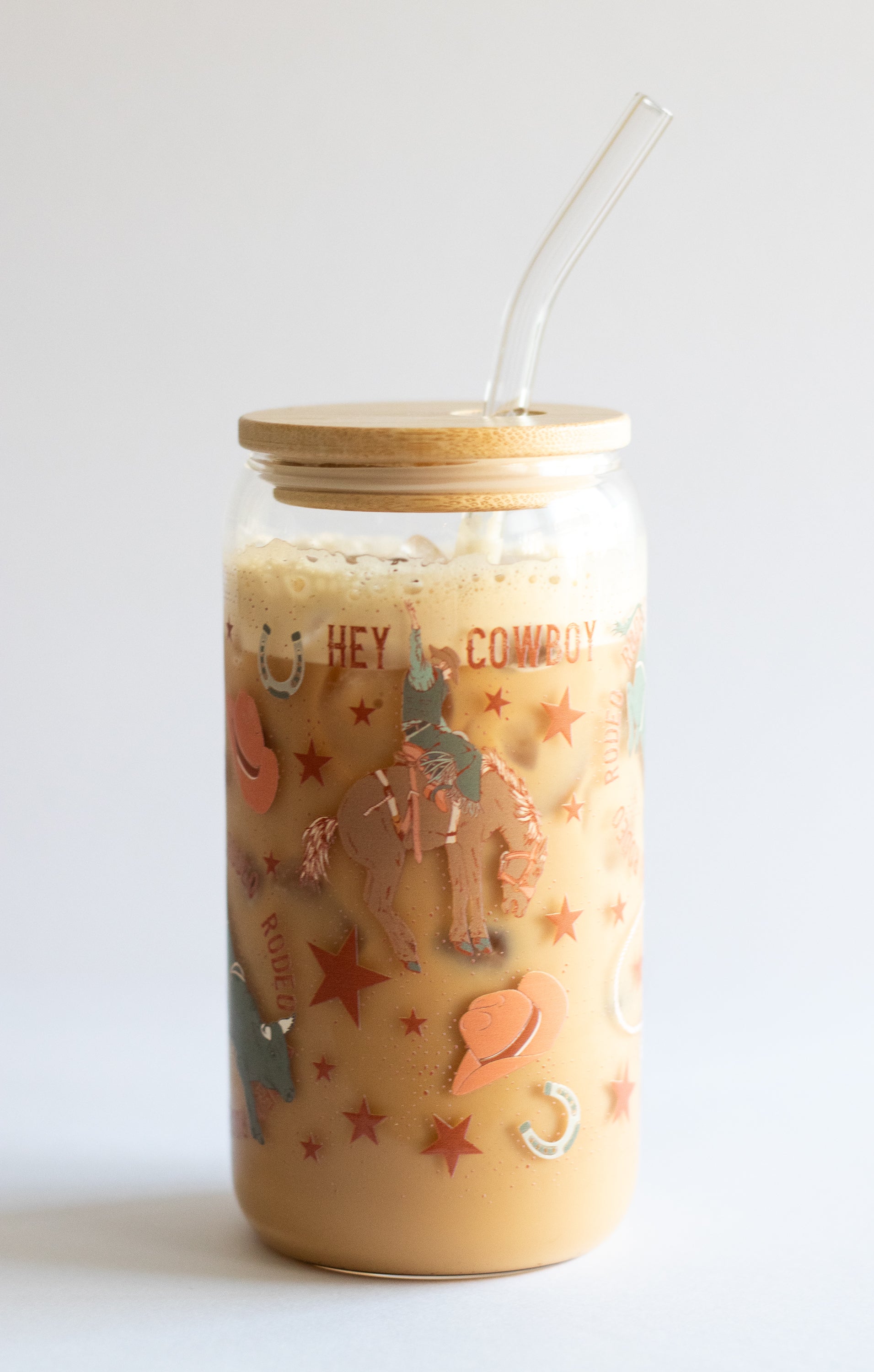 A can glass tumbler with a cowboy-themed design, bamboo lid, and a glass straw on a white background