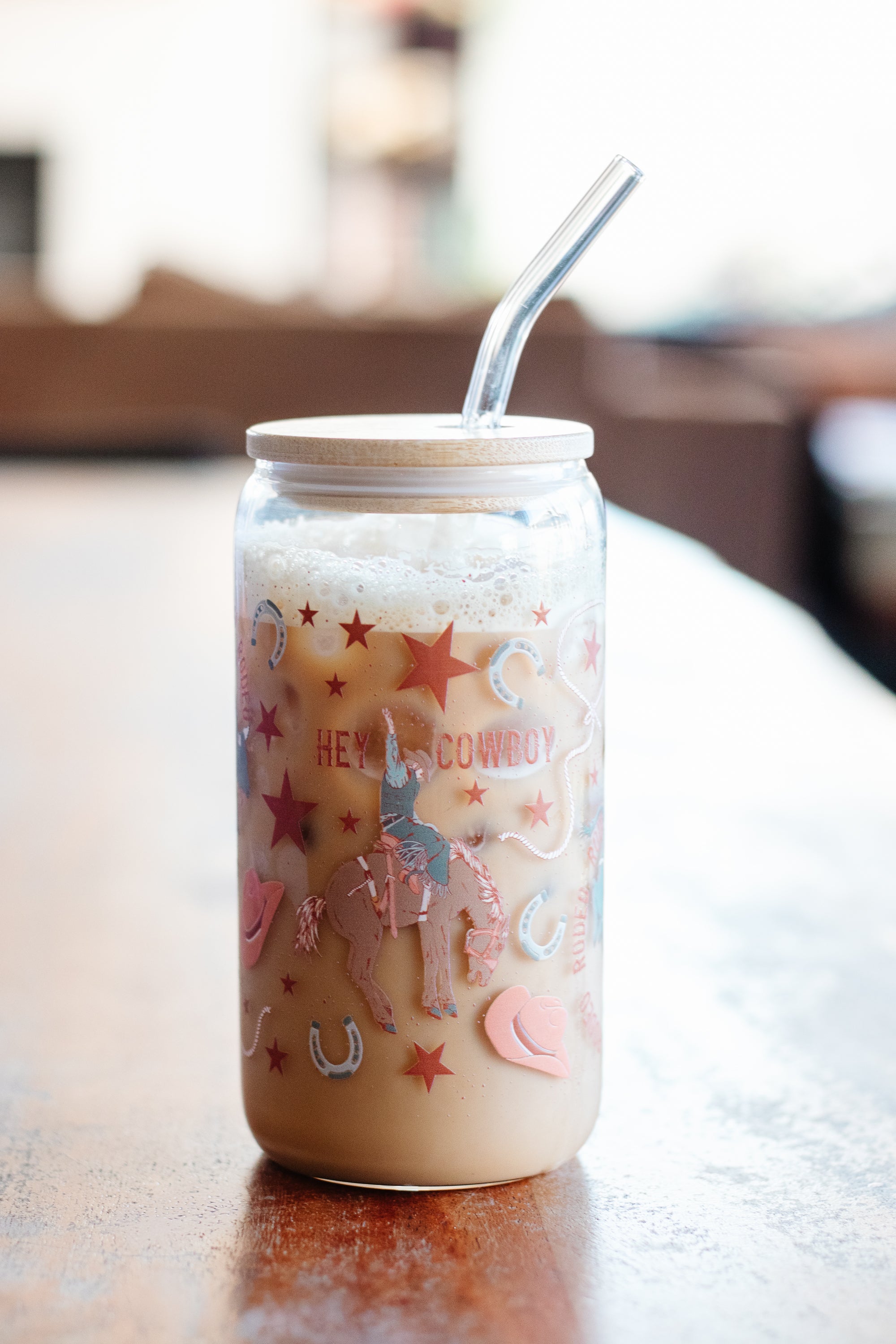 A can glass tumbler with a cowboy-themed design on a wooden surface and a blurred background