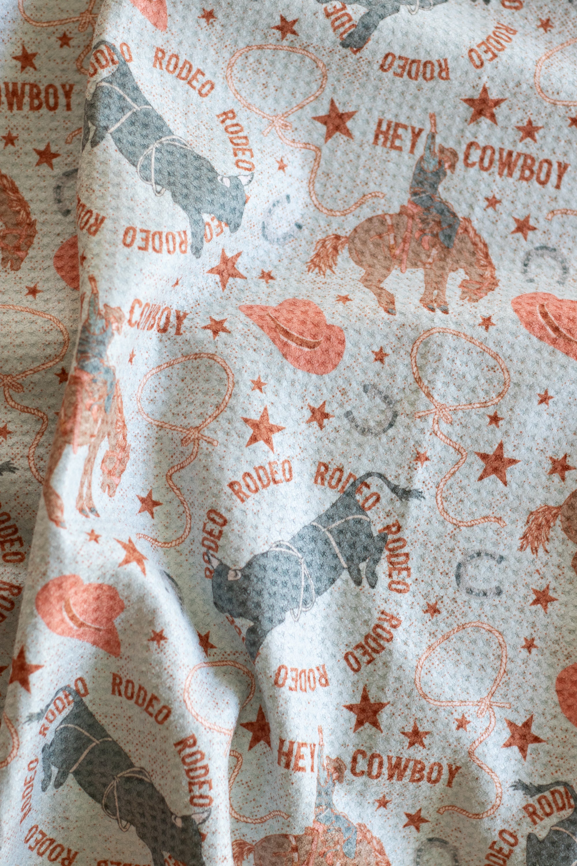 A waffle-weave kitchen tea towel with a cowboy and rodeo design on a light blue background