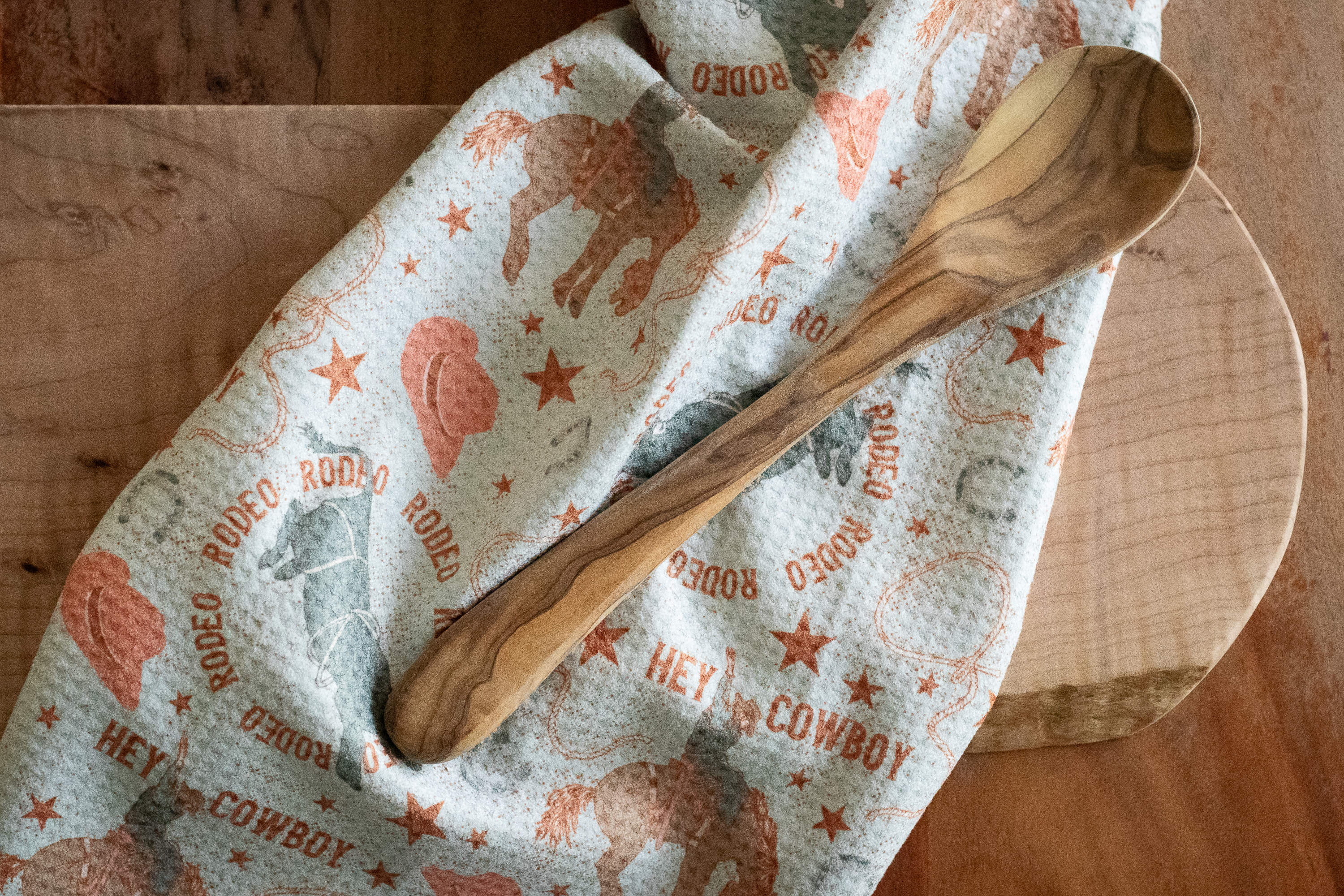 Wooden spoon on a cowboy-themed waffle-weave kitchen tea towel with a wooden surface underneath