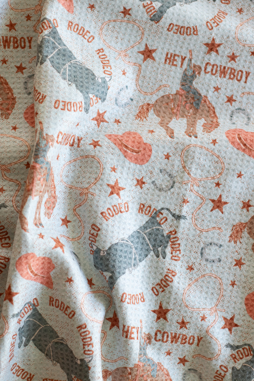 A waffle weave tea towel with cowboy and rodeo graphics on a light blue background 