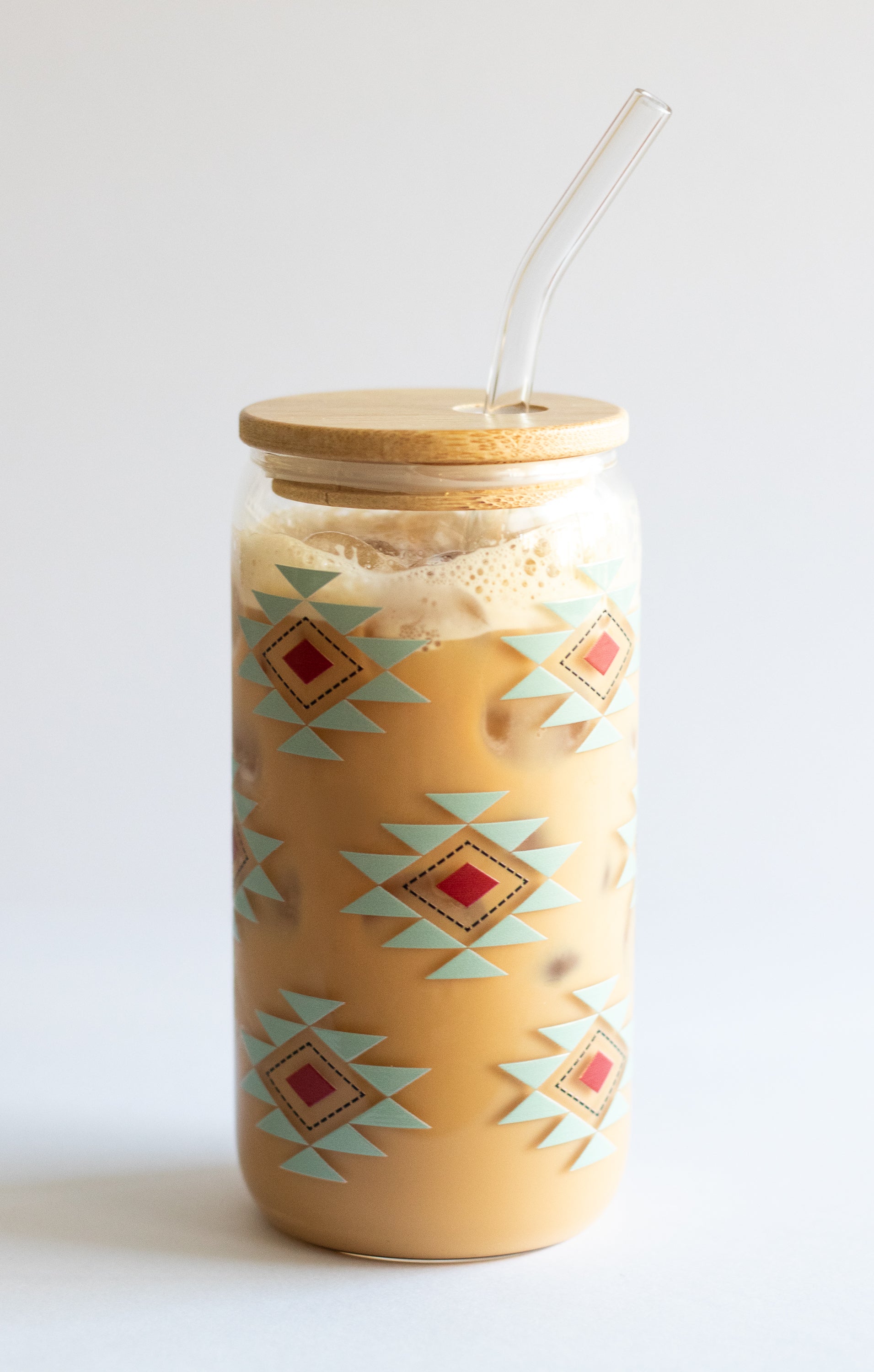 Can glass with a southwestern geometric pattern, a bamboo wooden lid, and a glass straw on a white background