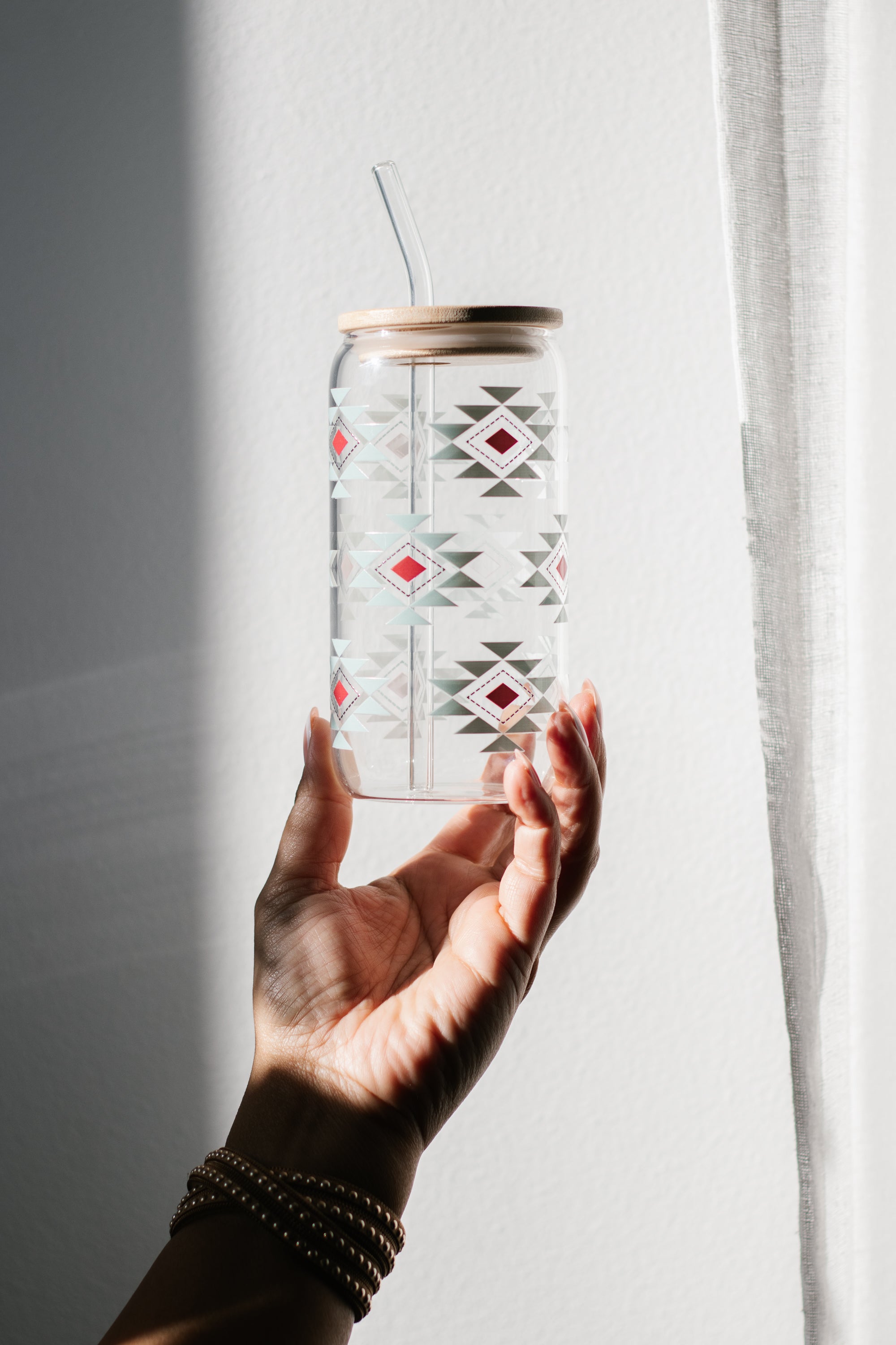 Hand holding a clear can glass with a southwestern geometric pattern against a light background