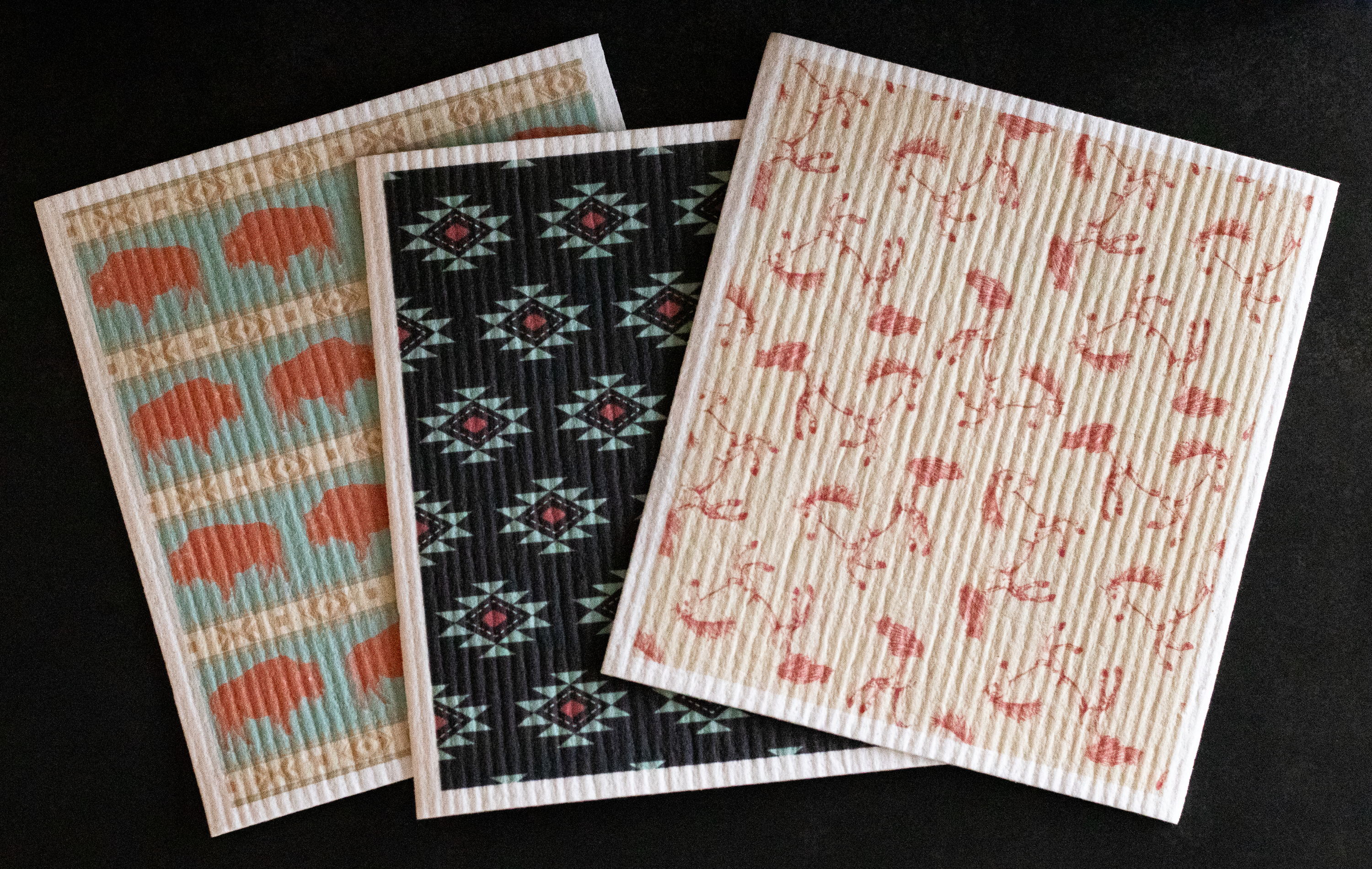 Three western-patterned Swedish dishcloths on a black background