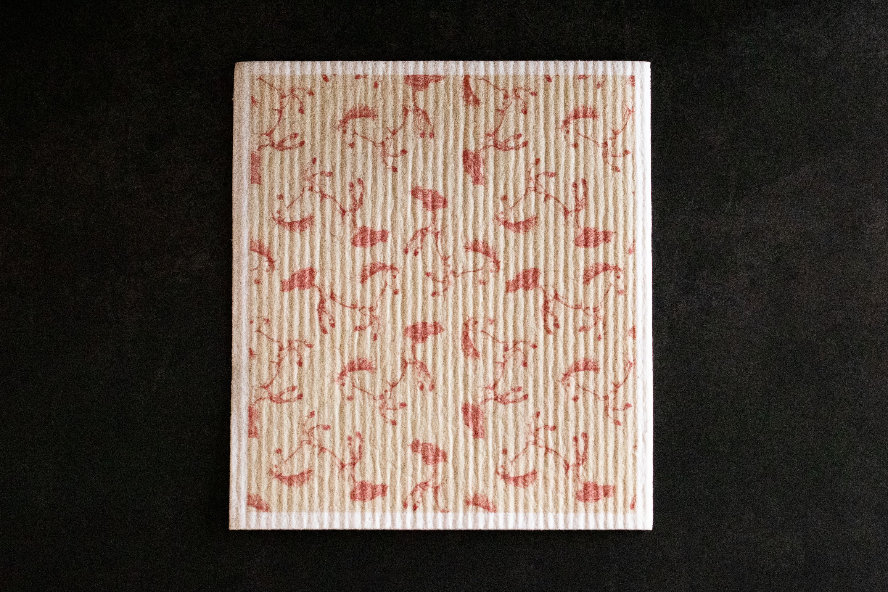 A patterned Swedish dishcloth with a red horse pattern on a black background