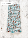 A waffle-weave kitchen tea towel with a western tooled leather floral pattern in shades of light blue and terracotta, folded lengthwise in half, on a textured white surface with a Bestseller label.
