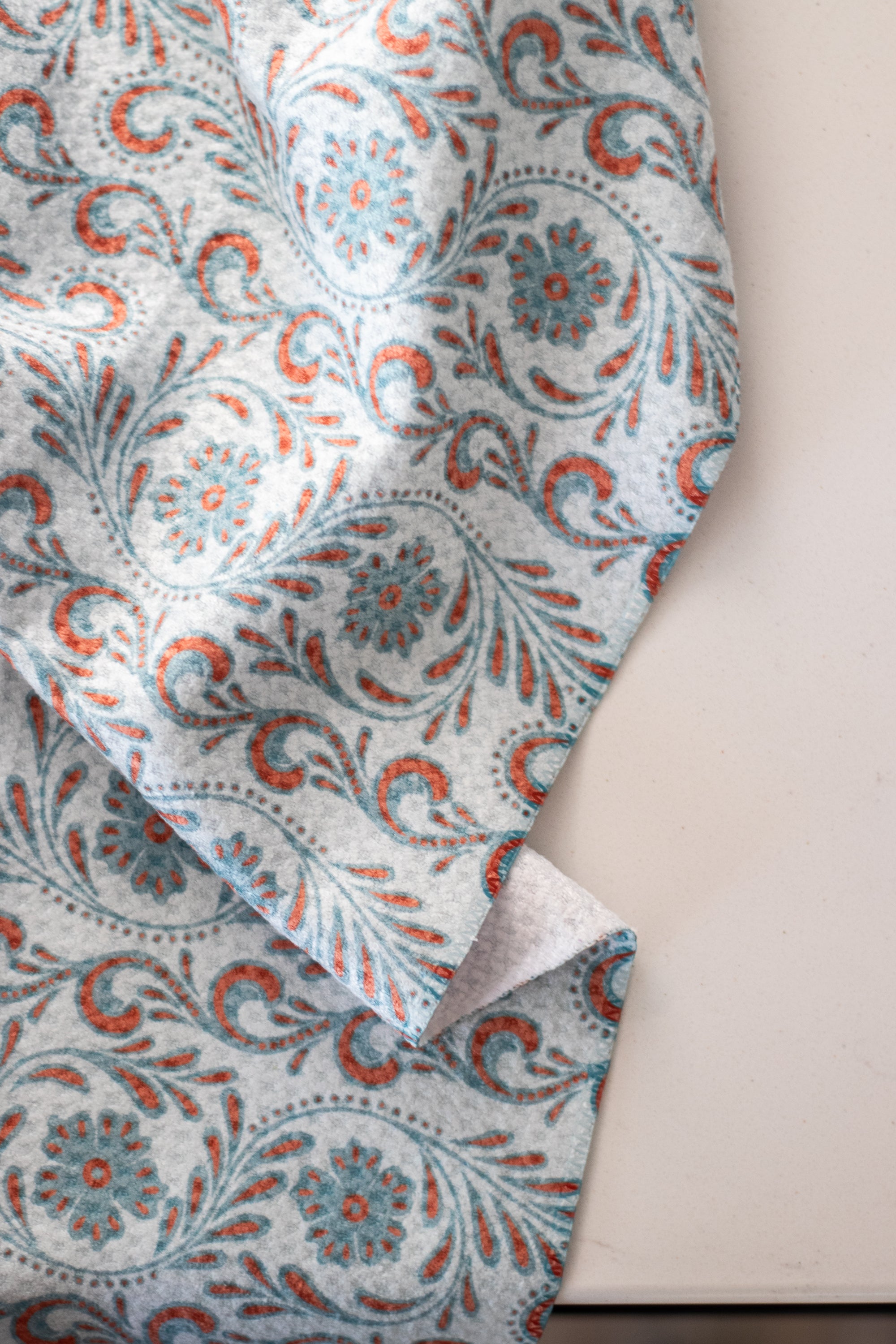 Close-up of a waffle-weave kitchen tea towel with a blue and terracotta-colored, tooled leather floral design on a white surface.